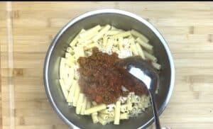 Pasta with meat sauce and cheese in a metal bowl on a wooden surface, ready to be mixed.